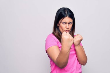 Genç, güzel, esmer, günlük pembe tişörtler giyen, beyaz arka planda duran, savunma hareketleriyle dövüşmeye hazır, kızgın ve üzgün yüzlü, problemden korkan bir kadın.