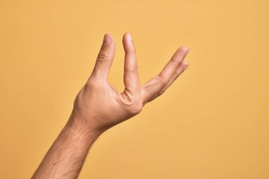 İzole edilmiş sarı arka plan üzerinde parmaklarını gösteren beyaz bir adamın eli. Görünmez bir şeyi alıp, parmaklarıyla uzayı gösteren bir nesneyi tutuyor.