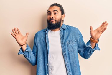 Gündelik giysiler giyen genç bir Arap, habersiz ve kolları açık, hiçbir fikrim yok ve şüpheli bir yüzüm var.. 