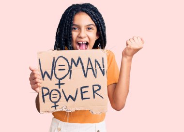 Sevimli Afro-Amerikan kızı elinde kadın güç pankartı tutarak gururla bağırıyor zaferi ve başarıyı kutluyor. 
