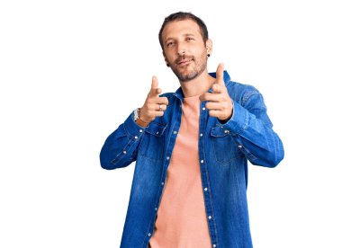 Gündelik giysiler giymiş genç yakışıklı adam mutlu ve komik yüzüyle kamerayı işaret ediyor. iyi enerji ve titreşimler. 