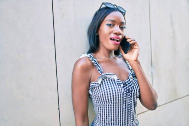 Genç Afrikalı Amerikalı kadın akıllı telefondan konuşuyor. Şehrin caddesinde duvara yaslanıyor.