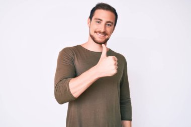 Gündelik giysiler giyen genç yakışıklı adam elleriyle mutlu bir jest yapıyor. Kameraya bakıp başarıyı gösteren ifade. 