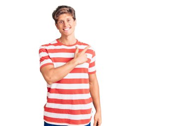 Genç, yakışıklı, günlük kıyafetler giyen, neşeli, yüzünde mutlu ve doğal bir ifadeyle, elleri ve parmaklarıyla işaret eden bir gülümseme olan bir adam. 