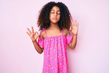 Kıvırcık saçlı, rahat giyinen, gözleri kapalı gülümseyen ve parmaklarıyla meditasyon yapan Afro-Amerikan çocuğu. yoga konsepti. 
