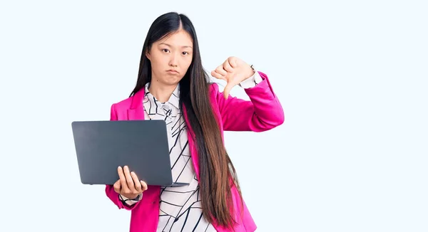 年轻美丽的中国女人使用脸色苍白的笔记本电脑 消极的标志表示不喜欢大拇指朝下 拒绝的观念 — 图库照片