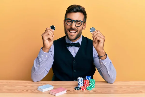 Handsome Hispanic Croupier Man Sitting Table Holding Casino Chips Winking — Stock Photo, Image