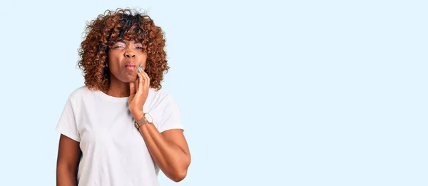 歯の痛みや歯の病気のため 若いアフリカ系アメリカ人女性は痛みを伴う表現で手で手に触れるカジュアルな白いTシャツを着ています 歯科医 — ストック写真