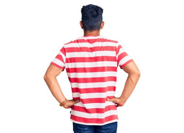 Yakışıklı Latin Amerikalı genç adam gündelik kıyafetler ve gözlük takıyor geriye bakıyor kollarını vücuduna dikiyor. 