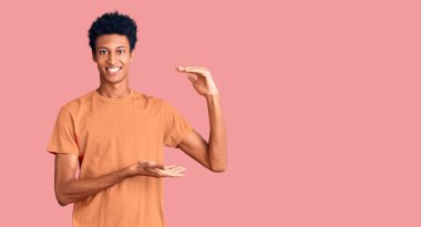 Genç Afrikalı Amerikalı sıradan kıyafetler giyen, elleri büyük ve büyük boy işareti gösteren, ölçü sembolü olan bir adam. Kameraya bakıp gülümsüyor. ölçüm kavramı. 