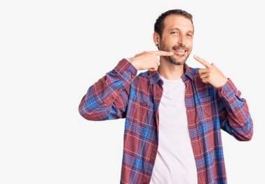 Gündelik kıyafetler giyen, neşeli gülümseyen, parmaklarıyla ve ağzıyla işaret eden genç yakışıklı bir adam. diş sağlığı kavramı. 