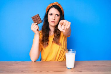 Çikolata yiyen ve bir bardak süt içen genç, güzel esmer kadın kamerayı işaret ediyor ve sen ciddi görünüyorsun. 