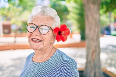 Yaşlı yaşlı, gri saçlı, dışarıda mutlu gülümseyen, dekoratif bir çiçek takan yaşlı kadın.