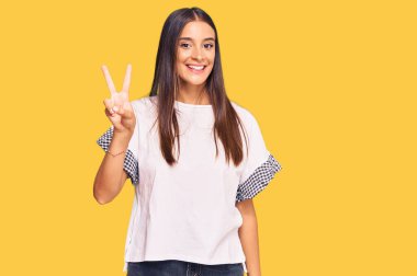 Genç İspanyol kadın gündelik giysiler giyiyor. İki numarayı gösterip işaret ediyor. Kendinden emin ve mutlu bir şekilde gülümsüyor.. 