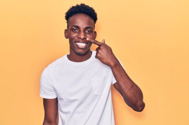 Genç Afro-Amerikan adam, günlük kıyafetler giyip, el ve burunla işaret ederek, neşeyle gülümsüyor. güzellik konsepti 