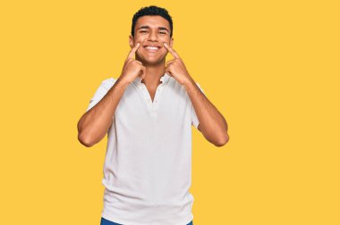 Gündelik kıyafetler giyen genç Arap adam ağzı açık gülümsüyor, parmakları işaret ediyor ve neşeli bir gülümseme sergiliyor. 