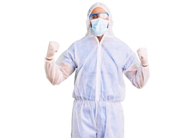 Koronavirüs üniforması ve sağlık maskesi takan genç İspanyol adam kollarını kaldırarak ve açık gözlerle başarıyı kutluyor ve şaşırıyor. Kazanan konsept. 