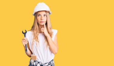 Güzel beyaz kadın, sarı saçlı, başlık takan ve inşaatçı kıyafetleri giyen. Ciddi yüzlü, eli çenesinde soru soran, kafa karıştırıcı bir fikir. 