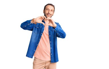 Gündelik kıyafetler giyen, aşık gülümseyen ve elleriyle kalp sembolü çizen genç yakışıklı bir adam. romantik kavram. 