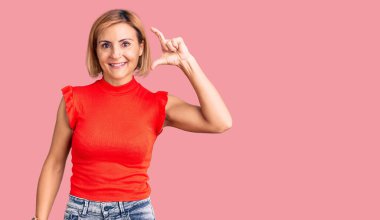 Gündelik kıyafetler giyen, gülümseyen, kendine güvenen, el hareketleriyle küçük beden işareti yapan, parmaklarını gösterip kameraya bakan genç sarışın kadın. ölçüm kavramı. 