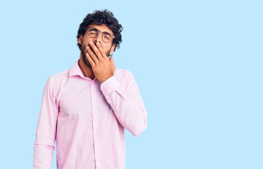 Kıvırcık saçlı ve iş kıyafetleri giyen yakışıklı genç adam ağzıyla esnemekten sıkılmış. Huzursuz ve uykulu.. 