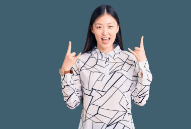 Genç, güzel, Çinli bir kadın, gündelik tişört giymiş, çılgın bir ifadeyle bağırıyor, elleri havada rock sembolü yapıyor. Müzik yıldızı. ağır müzik konsepti. 