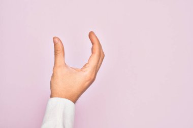 İzole edilmiş pembe arka plan üzerinde parmaklarını gösteren beyaz bir adamın eli. Görünmez bir şeyi alıp, parmaklarıyla uzayı gösteren bir nesneyi tutuyor.