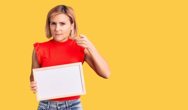 Elinde boş beyaz karatahta tutan genç sarışın kadın kamerayı işaret ediyor ve sen kendine güvenen, ciddi görünüyorsun. 