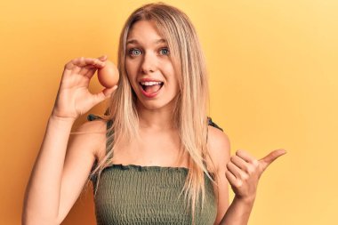 Sarışın genç bir kadın yumurta tutarken başparmağını yan tarafa uzatıyor ve ağzı açık gülümsüyor. 