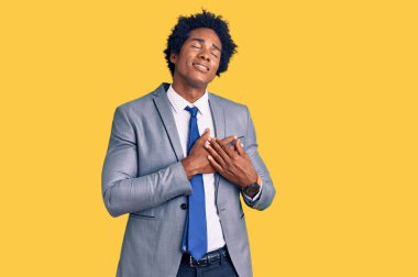 Afro saçlı, iş ceketi giyen, göğsünde elleri kapalı, yüzünde minnet ifadesi olan yakışıklı Afro-Amerikan bir adam. sağlık kavramı. 