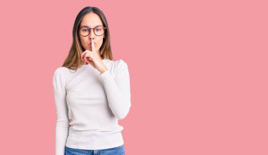 Güzel esmer, beyaz süveter giyen, gözlüklü, dudakları parmaklı, sessiz olmak isteyen bir kadın. sessizlik ve gizli konsept. 