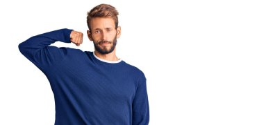 Sakallı yakışıklı, sıradan bir süveter giyen güçlü kol kası gösteren, kendinden emin ve gururlu bir adam. 