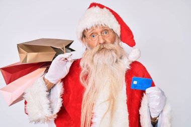 Noel Baba kostümü giyen yaşlı bir adam elinde alışveriş çantaları ve kredi kartı bilgisiz ve kafası karışık bir ifade tutuyor. şüphe kavramı. 