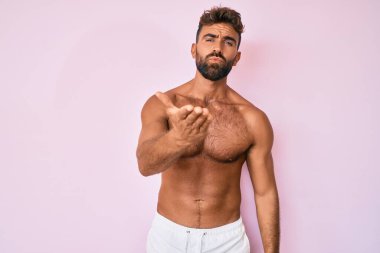 Latin asıllı genç adam kameraya üstsüz bir şekilde bakıyor ve havada bir öpücük savuruyor. Güzel ve seksi. aşk ifadesi. 