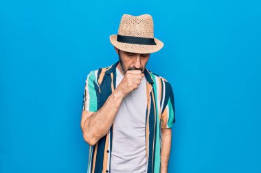 Mavi arka planda tişört ve şapka takan orta yaşlı yakışıklı turist kendini iyi hissetmiyor ve soğuk algınlığı veya bronşitin belirtisi olarak öksürüyor. Sağlık hizmeti kavramı.