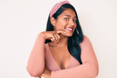 Uzun saçlı, rahat bir şekilde gülümseyen, kollarını kavuşturup çenesine dokunarak kameraya güvenen güzel Latin bir genç kadın. Olumlu düşünmek. 