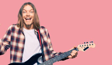 Uzun saçlı yakışıklı beyaz adam elektro gitar çalıyor gururla bağırıyor, zaferi ve başarıyı kutluyor kollarını kaldırarak çok heyecanlı 