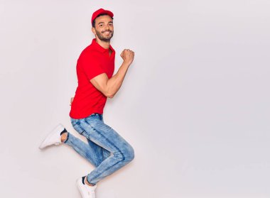 Mutlu gülümseyen üniformalı yakışıklı İspanyol teslimatçı. Yüzünde tebessümle zıplıyor, beyaz arka planda yumruklar havada kutluyor..