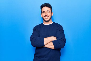 Gündelik kıyafetler giyen, kollarını kavuşturup kameraya gülümseyen genç İspanyol adam. pozitif kişi. 