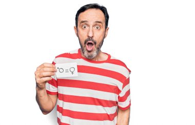 Orta yaşlı bir adam elinde eşit kadın ve erkek kavramına sahip kağıtlar tutarak şaşkınlık ve şaşkınlık içinde şaşkınlık içinde, şaşkınlık dolu bir ifade istiyor.