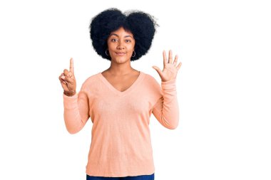 Genç Afro-Amerikan kızı gündelik giysiler giyip altı numaralı parmaklarıyla işaret ederken kendinden emin ve mutlu bir şekilde gülümsüyor.. 