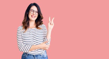 Güzel, genç, esmer bir kadın. Günlük kıyafetler ve gözlük takıyor. Gülümsüyor, kameraya göz kırpıyor ve zafer işareti yapıyor. İki numara.. 