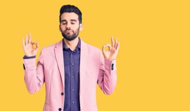 Zarif ceketli, sakallı, genç ve yakışıklı bir adam. Rahat ol ve gülümse. Gözleri kapalı, parmaklarıyla meditasyon hareketi yapıyor. yoga konsepti. 