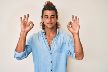 Yaz tarzı giyinen genç İspanyol adam rahatla ve gözleri kapalı gülümse parmaklarıyla meditasyon hareketi yapıyor. yoga konsepti. 