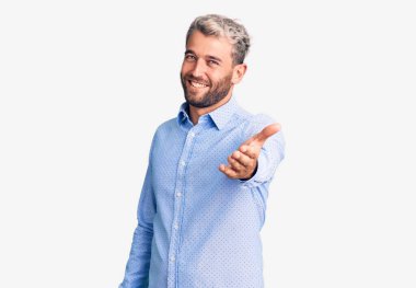Young handsome blond man wearing elegant shirt smiling cheerful offering palm hand giving assistance and acceptance.  clipart