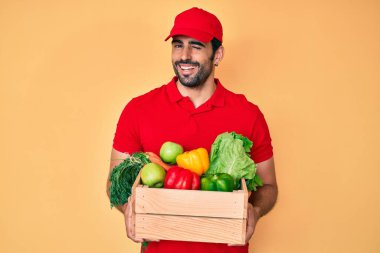 Yakışıklı, sakallı, üniformalı, teslimat yemeği taşıyan seksi bir ifadeyle kameraya bakan, neşeli ve mutlu yüzlü bir adam.. 