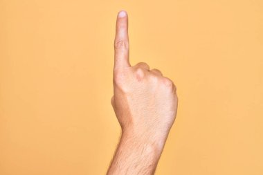 İzole edilmiş sarı arka planda parmaklarını gösteren beyaz bir gencin eli işaret parmağı kullanarak bir numarayı sayıyor, fikir ve anlayış gösteriyor.