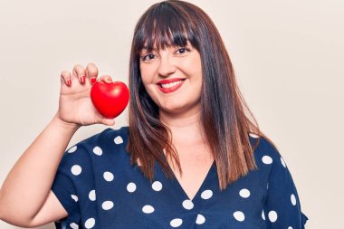 Kalbini tutan genç ve iri yarı bir kadın. Pozitif ve mutlu görünüyor. Kendine güvenen bir gülümsemeyle ayakta duruyor ve dişlerini gösteriyor. 