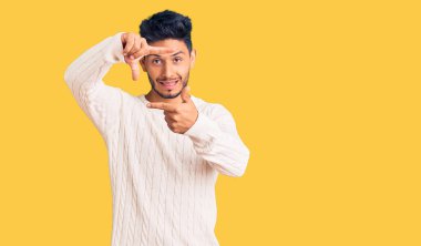 Yakışıklı Latin Amerikalı, sıradan bir süveter giyen, gülümseyen, elleri ve parmakları gülen yüzlü, çerçeveli bir genç. yaratıcılık ve fotoğrafçılık kavramı. 