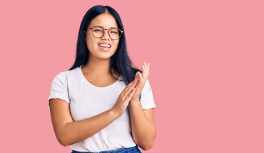 Genç, güzel Asyalı kız, günlük kıyafetler ve gözlük takıyor, alkışlıyor, mutlu ve neşeli alkışlıyor, gururla gülümsüyor. 